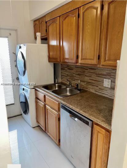 kitchen with stainless steel dishwasher, tasteful backsplash, stacked washing maching and dryer, light tile patterned floors, and sink