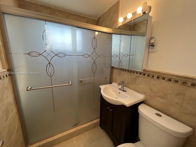 bathroom with a shower with shower door, tile patterned floors, vanity, tile walls, and toilet