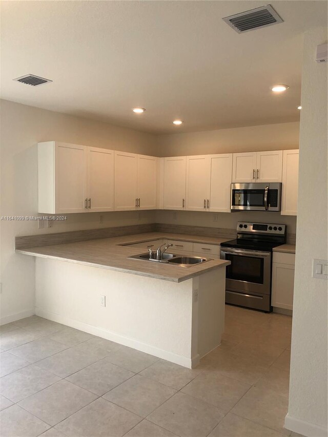 kitchen featuring appliances with stainless steel finishes, sink, white cabinets, light tile patterned floors, and kitchen peninsula