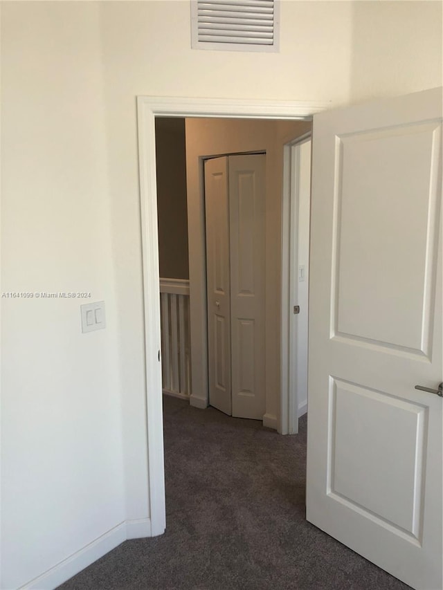 hallway with baseboards, visible vents, and dark carpet