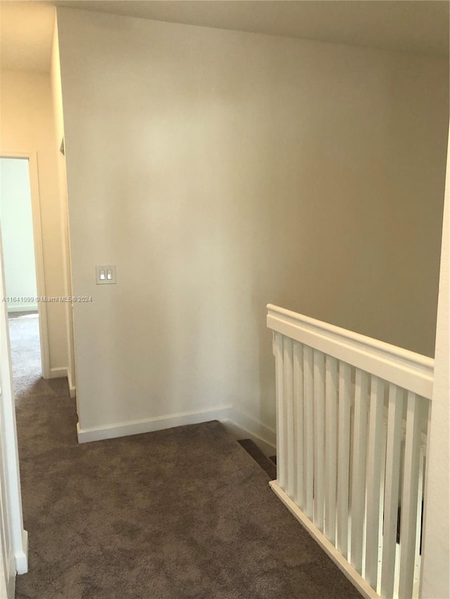 corridor with baseboards and dark colored carpet