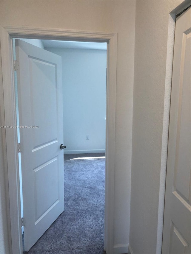 hallway featuring baseboards and dark colored carpet