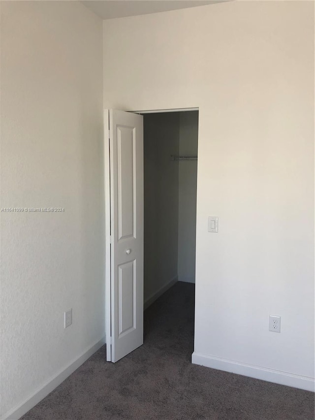 unfurnished bedroom featuring dark colored carpet, a closet, and baseboards