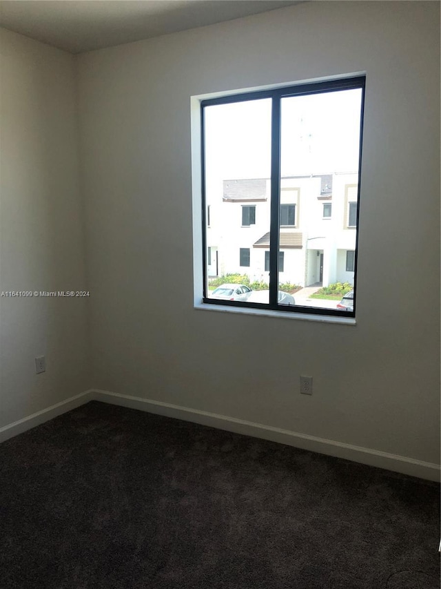 unfurnished room featuring baseboards and dark carpet