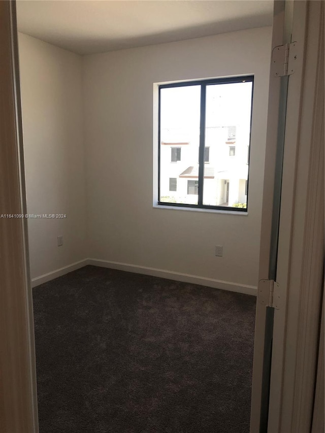 spare room with dark carpet and baseboards