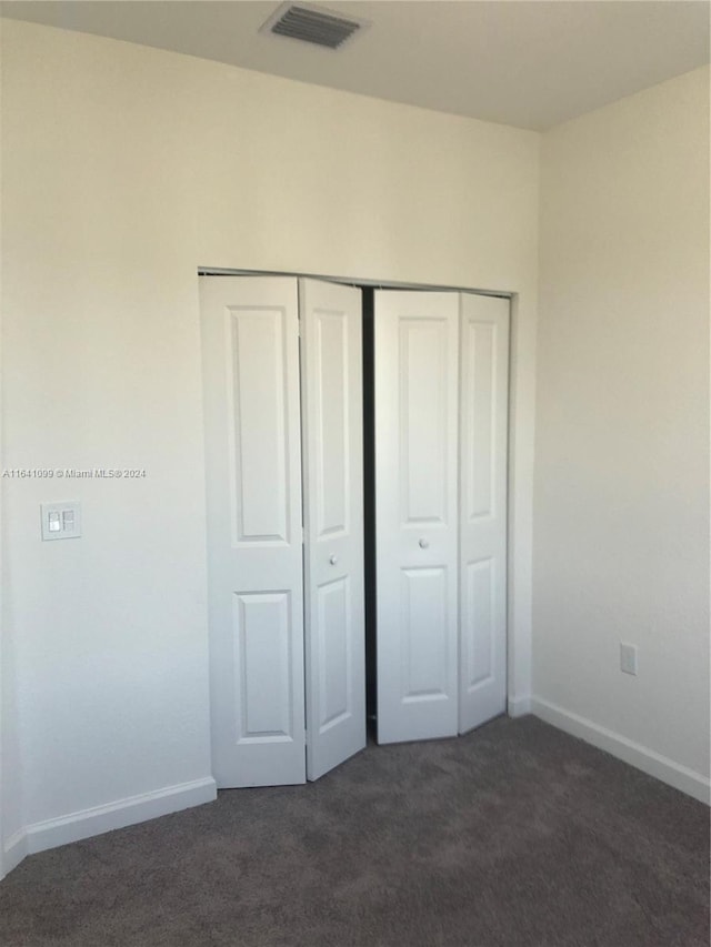 unfurnished bedroom with baseboards, visible vents, dark colored carpet, and a closet