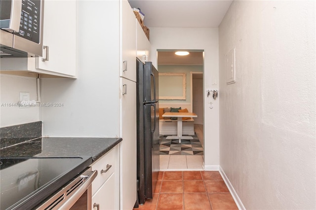 kitchen with light tile patterned floors, black refrigerator, dark stone counters, and white cabinets