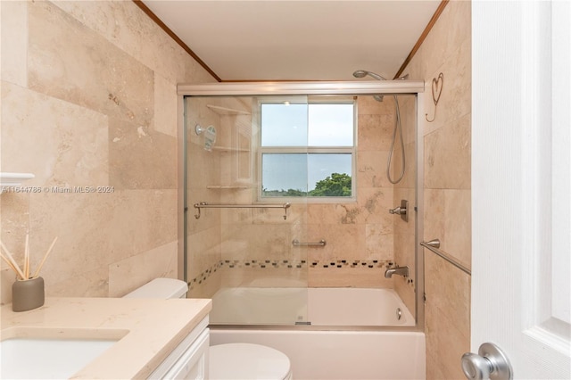 full bathroom featuring combined bath / shower with glass door, vanity, tile walls, crown molding, and toilet