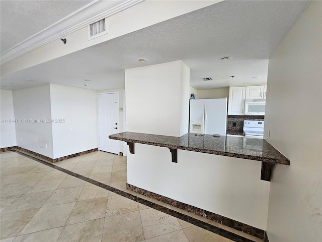 1650 Coral Way Unit 601, Miami, FL 33145 - kitchen with a kitchen breakfast bar, white appliances, white cabinets, dark stone countertops, and tasteful backsplash