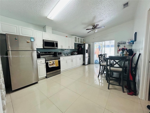 kitchen featuring white cabinetry, tasteful backsplash, lofted ceiling, light tile patterned flooring, and appliances with stainless steel finishes