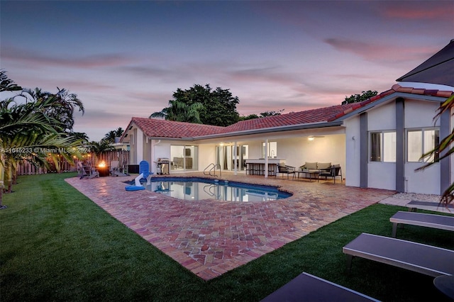 pool at dusk featuring a patio area and a lawn