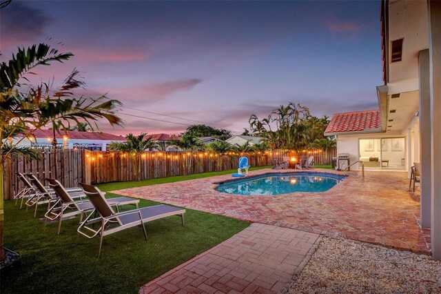 pool at dusk featuring a patio and a yard