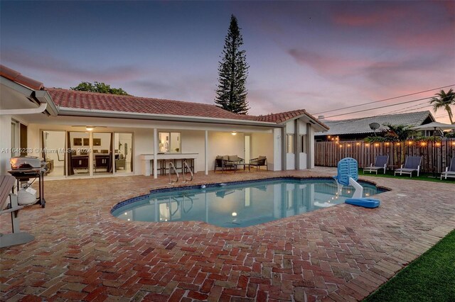 pool at dusk with a patio and area for grilling