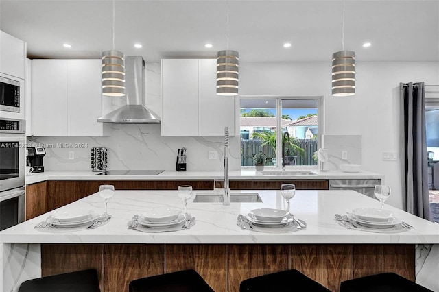 kitchen featuring backsplash, white cabinetry, a kitchen bar, wall chimney exhaust hood, and a center island with sink