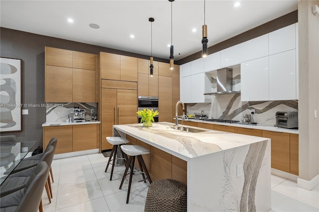 kitchen with backsplash, a kitchen bar, wall chimney exhaust hood, an island with sink, and white cabinets