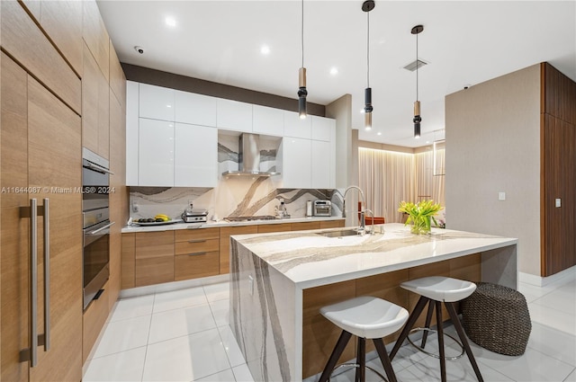 kitchen featuring a breakfast bar, backsplash, sink, wall chimney range hood, and white cabinets