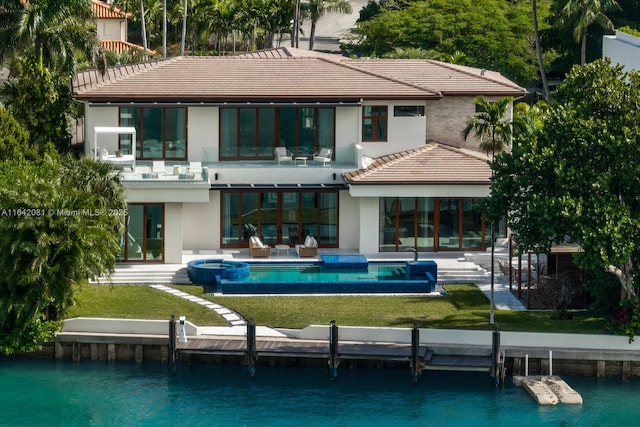 rear view of property featuring a lawn, a water view, a swimming pool with hot tub, a balcony, and a patio