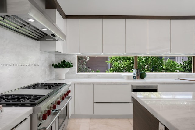 kitchen with high end stove, backsplash, white cabinetry, and wall chimney exhaust hood