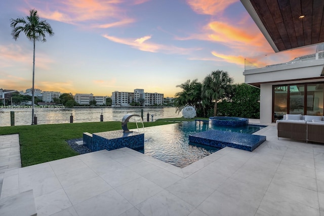 pool at dusk featuring an in ground hot tub, an outdoor hangout area, a water view, a patio area, and a lawn