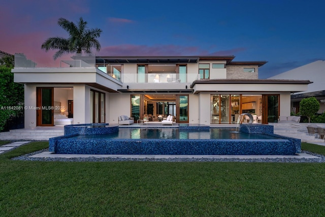 back house at dusk with a lawn, pool water feature, a balcony, and a patio