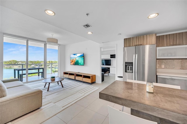 kitchen featuring stainless steel appliances, decorative backsplash, a water view, light tile patterned floors, and a wall of windows