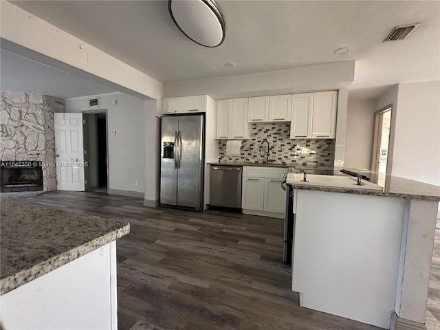 kitchen with white cabinetry, dark wood-type flooring, stainless steel appliances, backsplash, and a fireplace