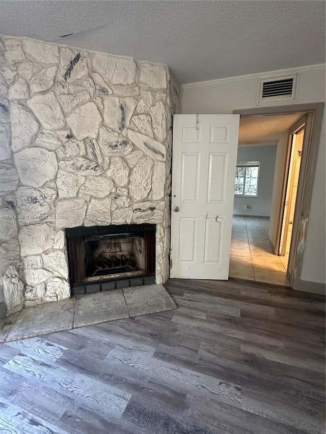 interior space with a stone fireplace, crown molding, a textured ceiling, and hardwood / wood-style flooring