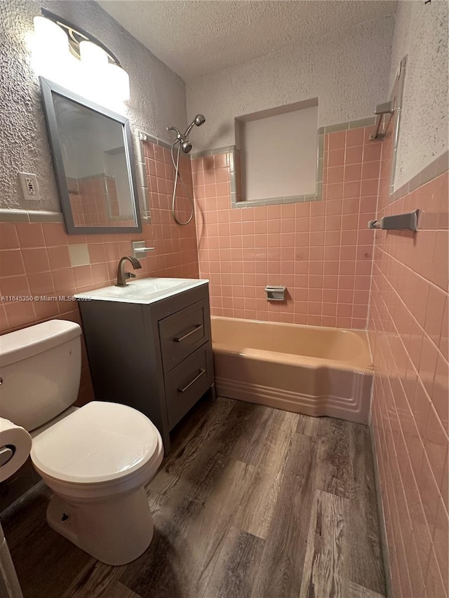 full bathroom with vanity, tiled shower / bath combo, a textured ceiling, tile walls, and wood-type flooring