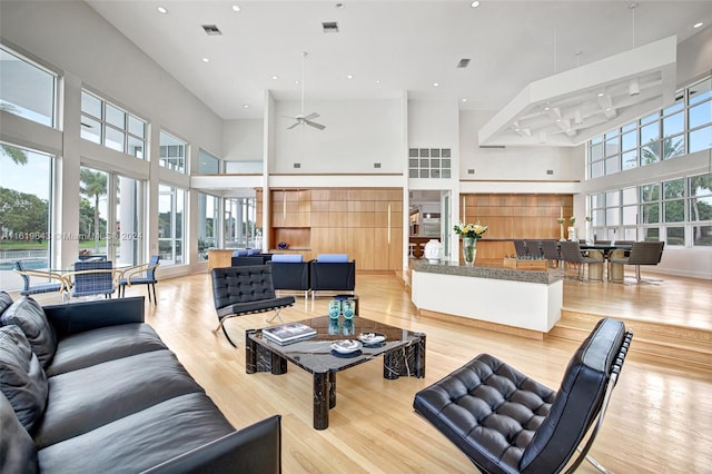 living room with ceiling fan, a towering ceiling, and light wood-type flooring