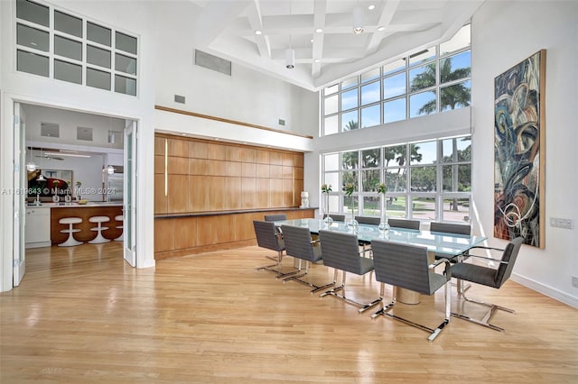 dining area with beam ceiling, coffered ceiling, a towering ceiling, and light hardwood / wood-style flooring