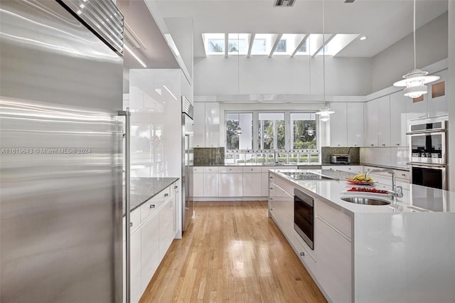 kitchen with stainless steel appliances, sink, decorative light fixtures, white cabinetry, and light hardwood / wood-style floors