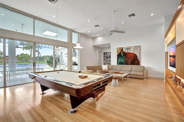 rec room with light hardwood / wood-style flooring, billiards, a water view, a towering ceiling, and ceiling fan