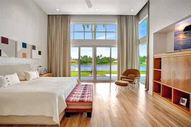 bedroom with ceiling fan, a towering ceiling, light hardwood / wood-style flooring, and access to exterior