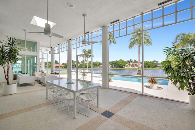 unfurnished sunroom featuring a water view, ceiling fan, a skylight, and plenty of natural light