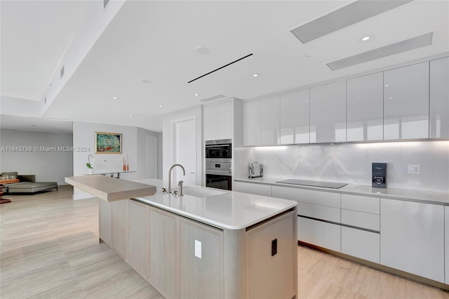 kitchen with decorative backsplash, white cabinetry, an island with sink, and double oven