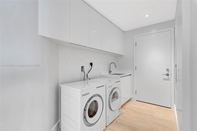 laundry area with washing machine and dryer, sink, light hardwood / wood-style flooring, and cabinets