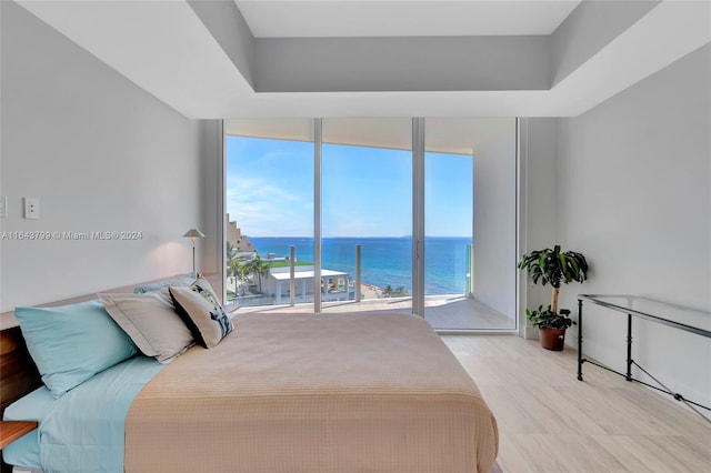 bedroom featuring a wall of windows, light hardwood / wood-style flooring, a water view, and access to outside