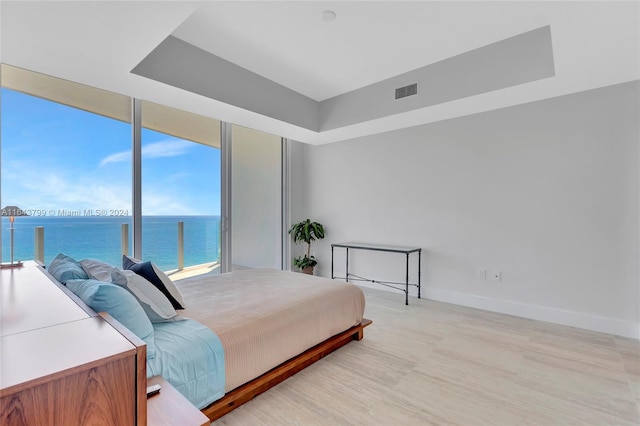 bedroom with light wood-type flooring, expansive windows, and a water view