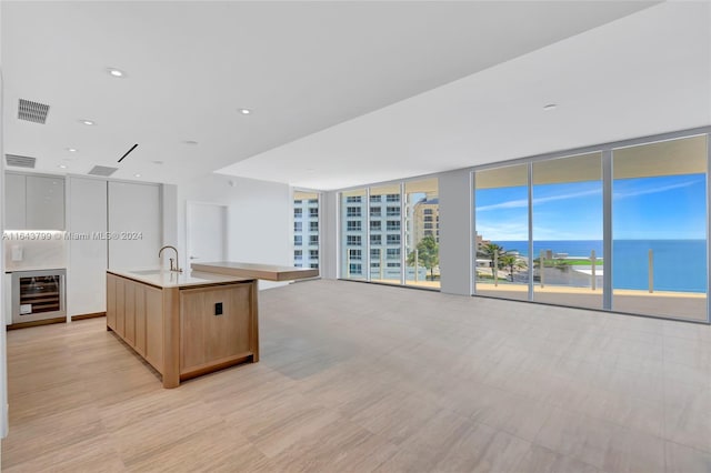 kitchen with sink, wine cooler, a water view, an island with sink, and expansive windows