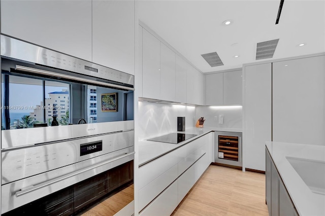 kitchen featuring light hardwood / wood-style flooring, stainless steel double oven, tasteful backsplash, beverage cooler, and white cabinets