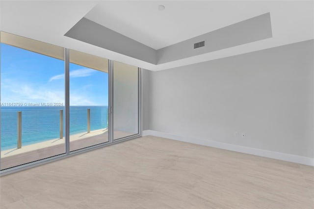 empty room featuring a water view, light tile patterned flooring, a healthy amount of sunlight, and a wall of windows