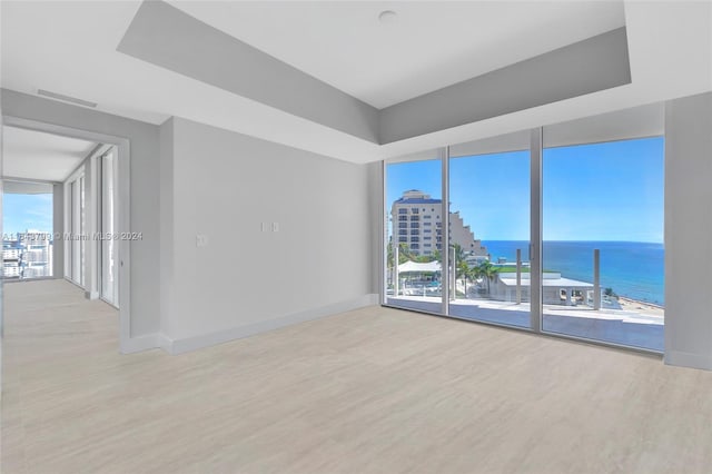 spare room featuring light wood-type flooring, floor to ceiling windows, and a water view