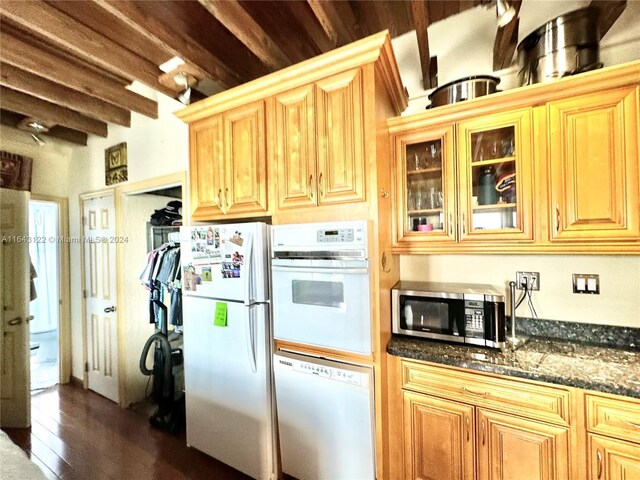 kitchen featuring white appliances, dark wood-type flooring, dark stone countertops, and beamed ceiling