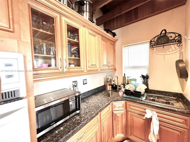 kitchen with dark stone counters, beam ceiling, sink, and stainless steel appliances