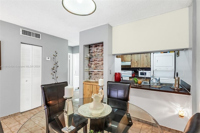 dining space featuring stacked washing maching and dryer, a textured ceiling, and light tile patterned floors