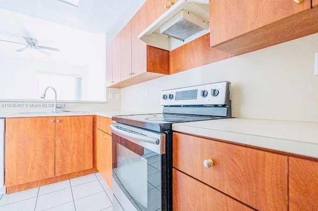 kitchen with stainless steel electric range, light countertops, under cabinet range hood, a sink, and light tile patterned flooring