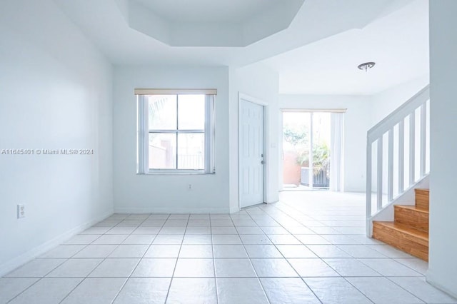 empty room with light tile patterned flooring and a raised ceiling