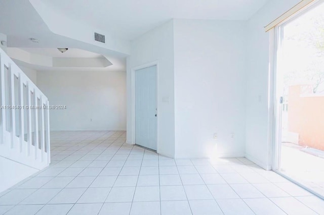 spare room with a tray ceiling, visible vents, and light tile patterned floors