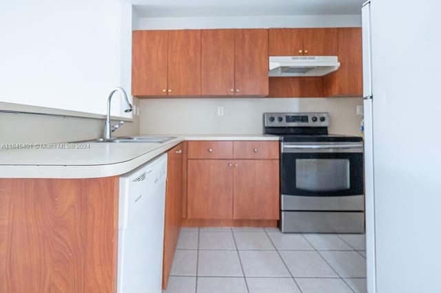 kitchen featuring light tile patterned floors, under cabinet range hood, white appliances, a sink, and light countertops