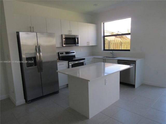 kitchen with appliances with stainless steel finishes, white cabinetry, sink, light tile patterned floors, and a kitchen island